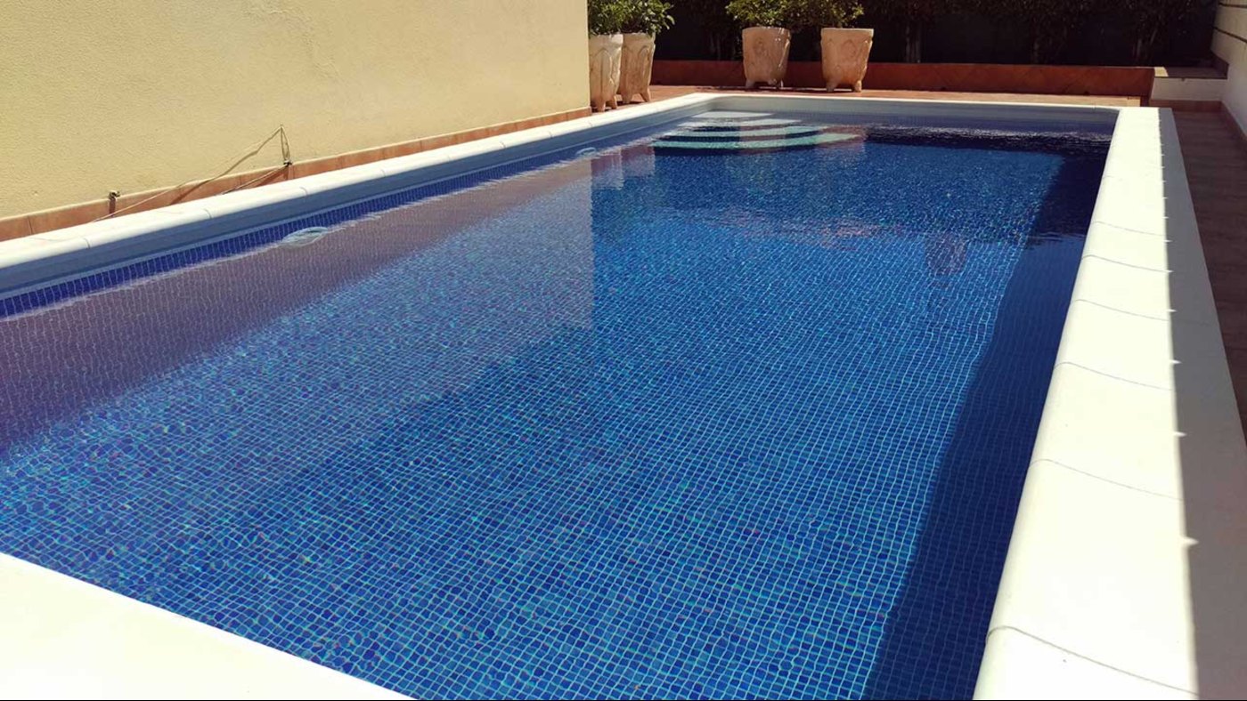 Piscina de hormigón terminada con gresite azul y coronación de piedra clara