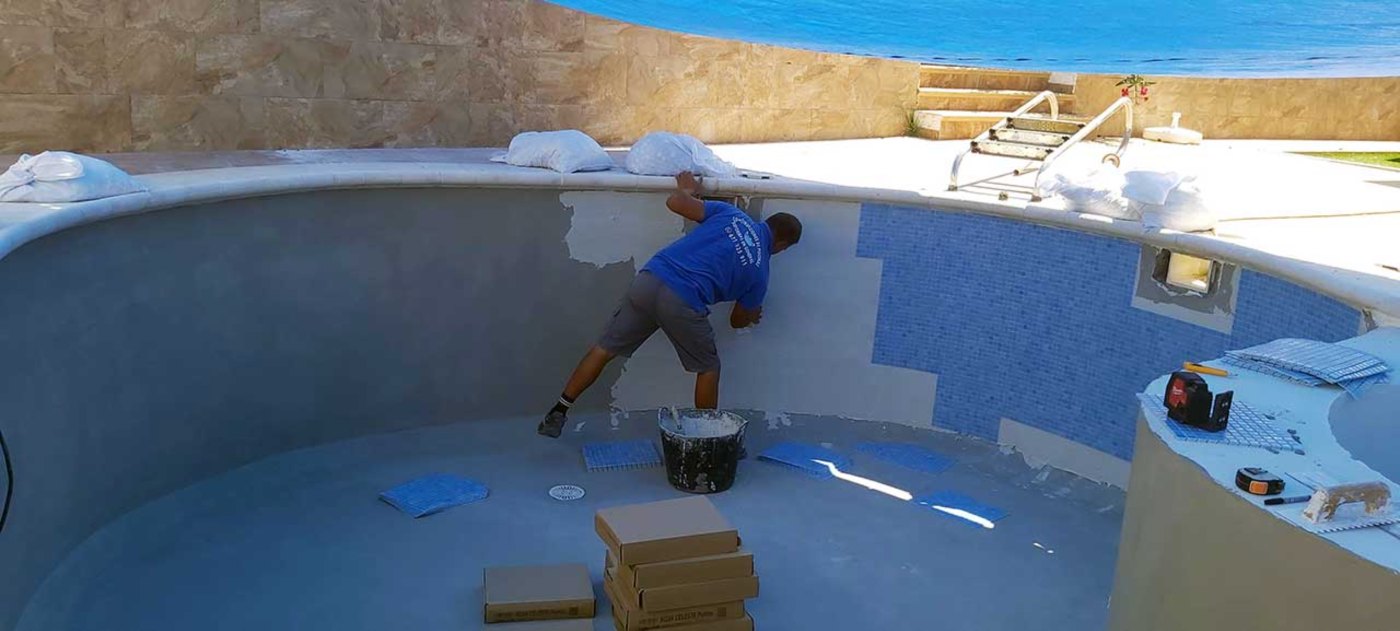 Operario colocando gresite azul en la pared de una piscina frente al mar