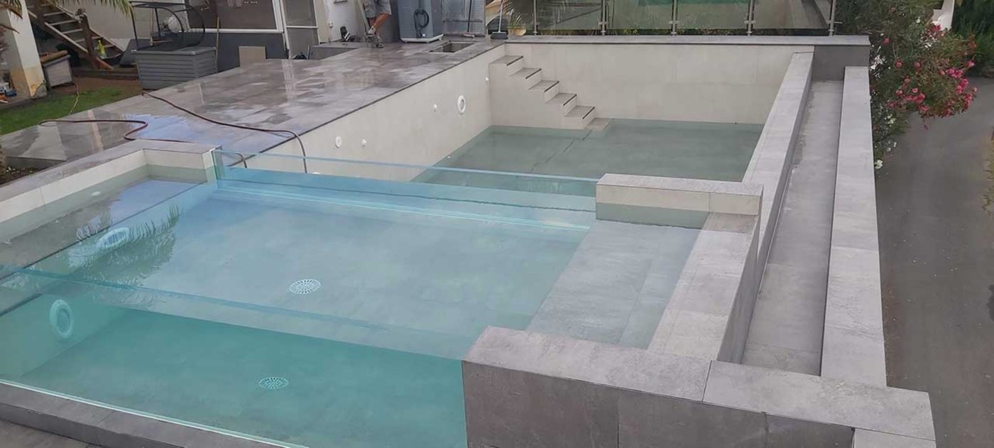 Piscina de hormigón con rebosadero recién llenada, con escaleras de obra y coronación de piedra gris